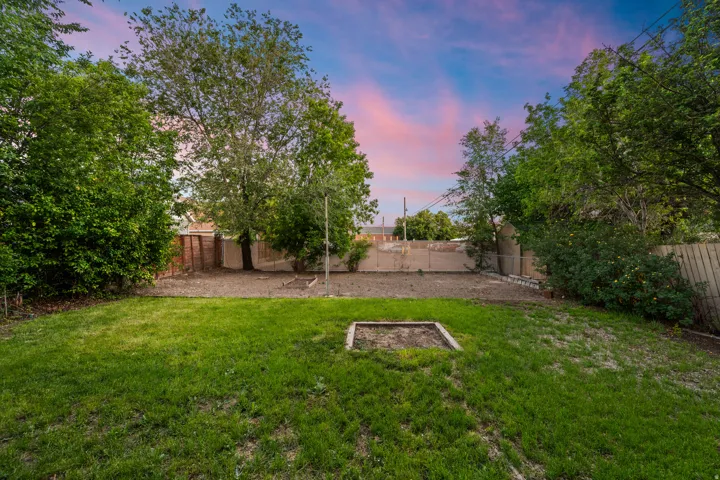 Spacious backyard featuring a manicured lawn, established trees, and a wooden perimeter fence