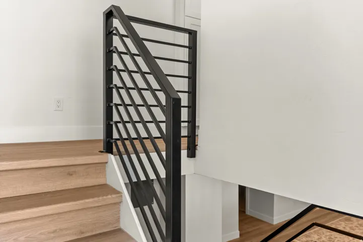 Staircase featuring light wood-finish treads and risers, white baseboards, and a contemporary black metal balustrade with horizontal railings