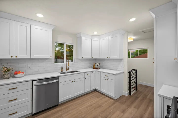Bright kitchen featuring white shaker cabinetry, white subway tile backsplash, stainless steel dishwasher, and a bronze-finish faucet