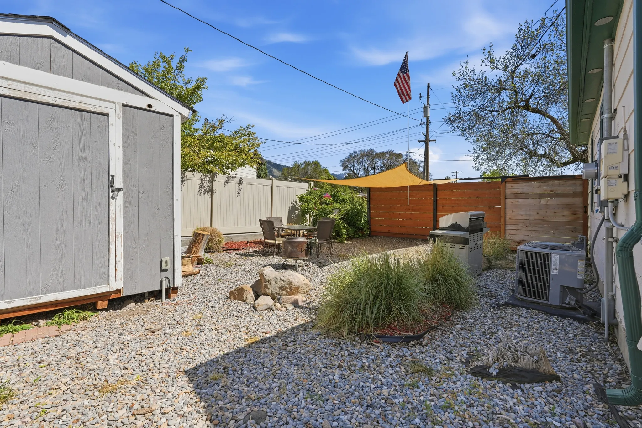 Gravel backyard with a grey storage shed, a wood-slat privacy fence, and an orange shade sail