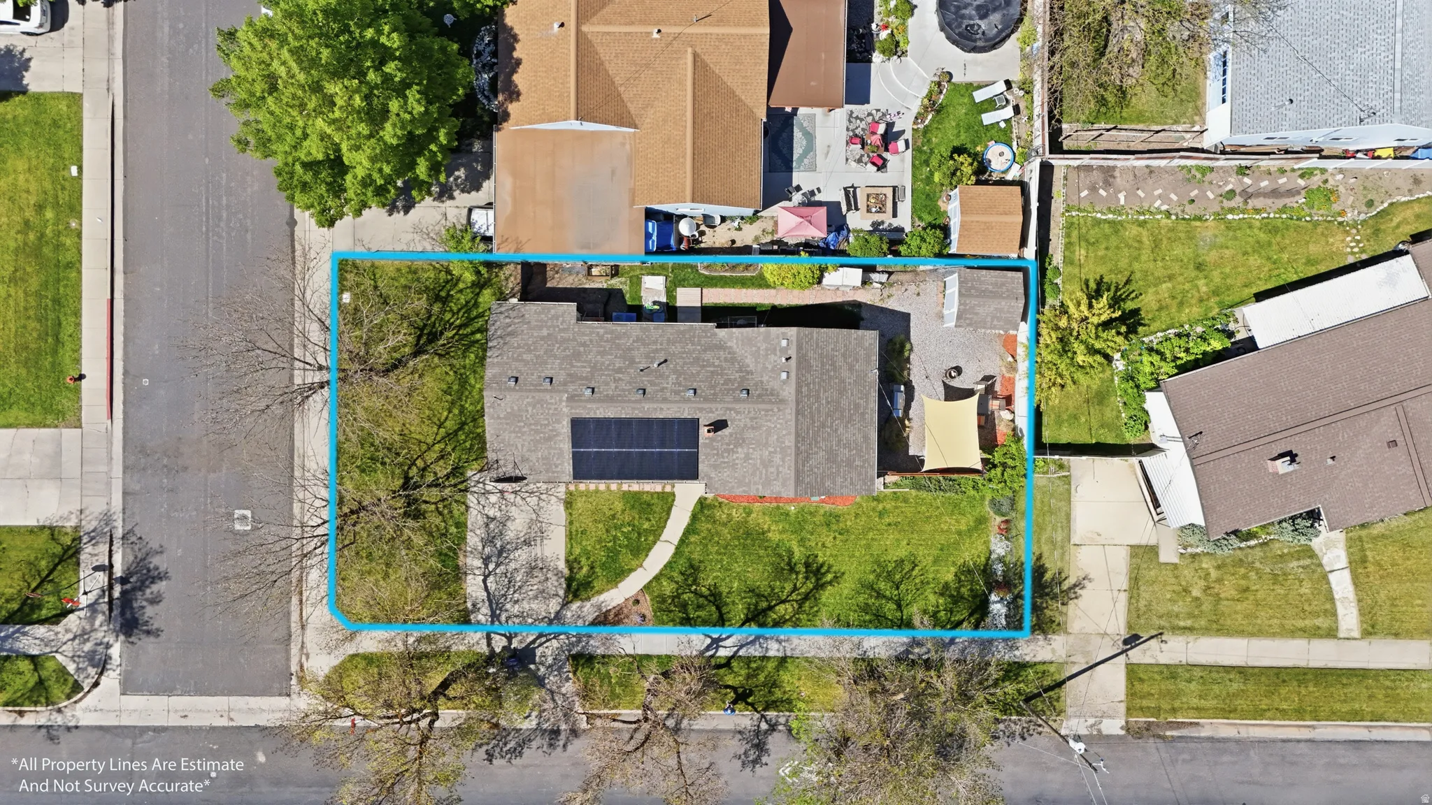 Property featuring a dark shingle roof with solar panels, a grass lawn, and mature trees