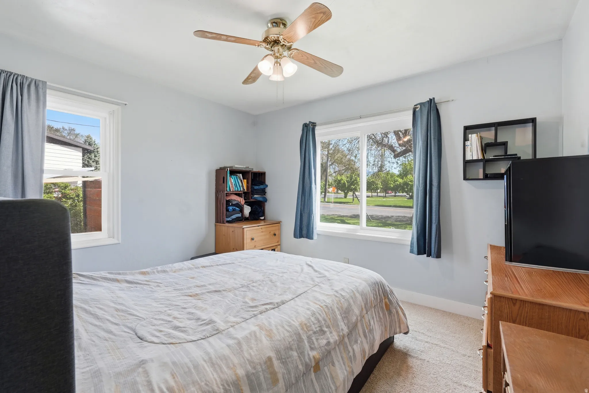 Bedroom featuring a ceiling fan with integrated lighting, two windows, and light-toned wall paint