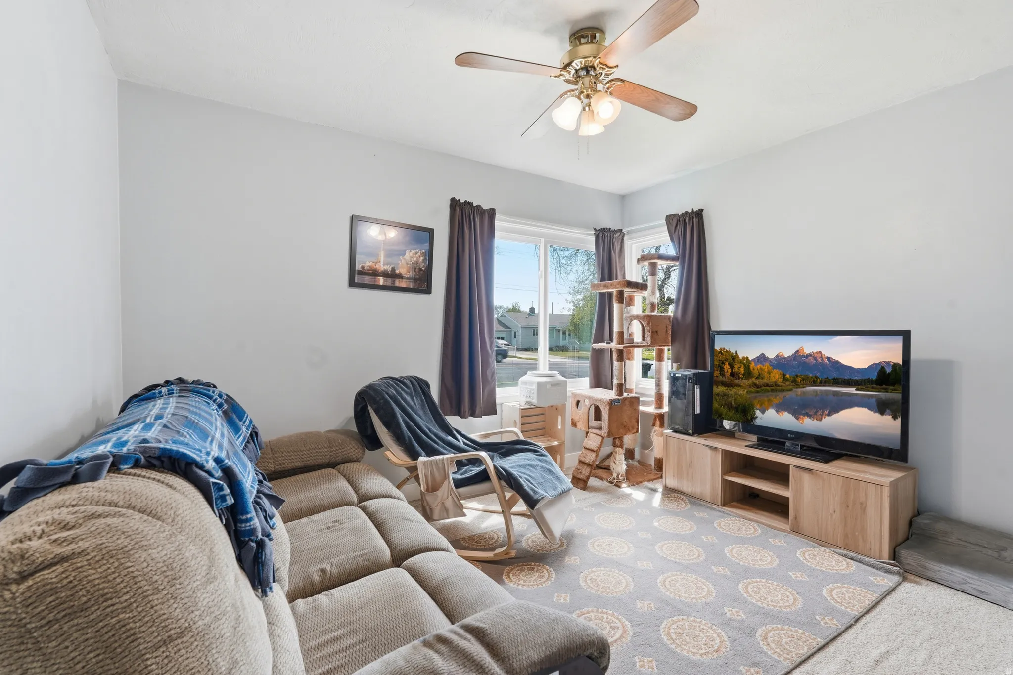 Living area featuring light gray walls, a ceiling fan with integrated lighting, and a large window with vertical blinds