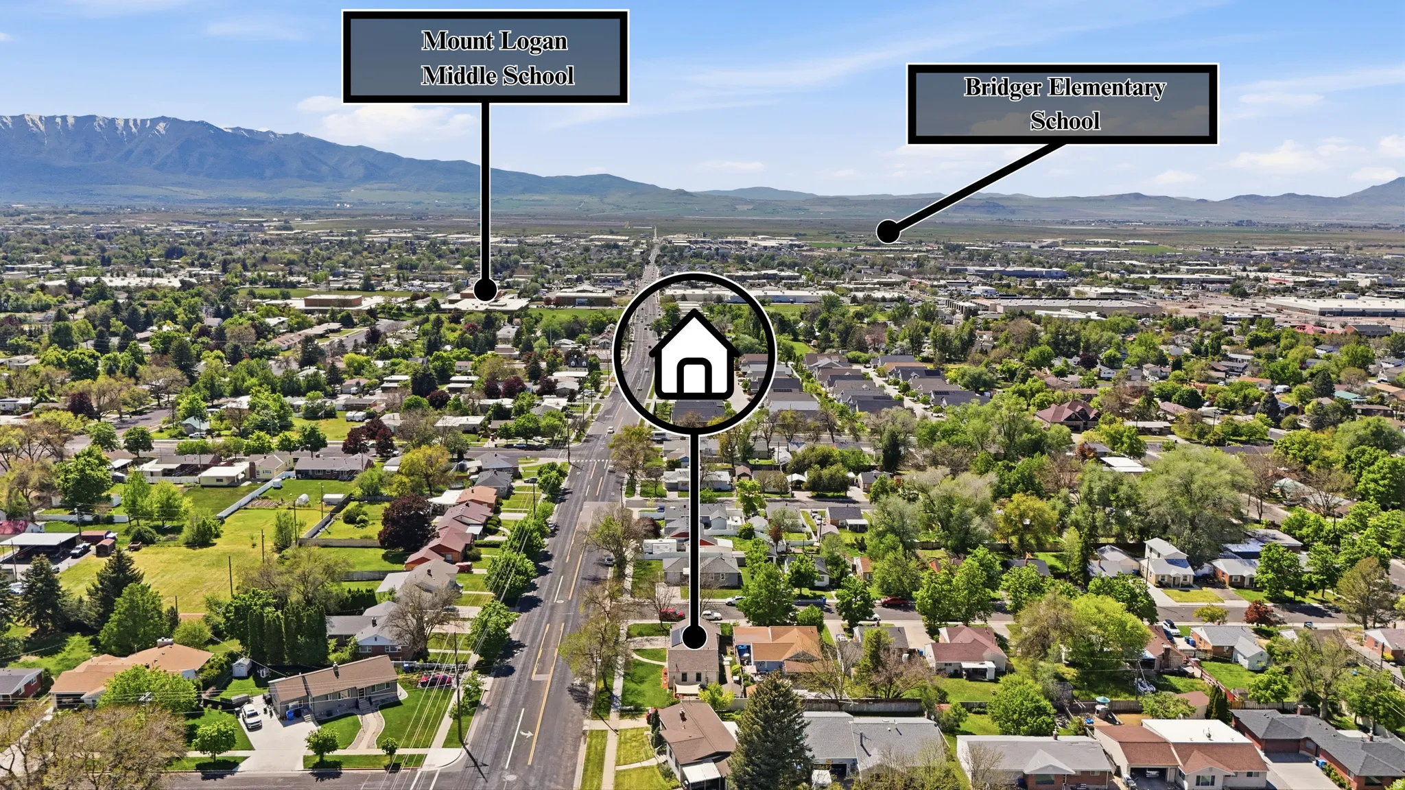 Aerial view showcasing a residential area with a prominent central thoroughfare, surrounded by mature trees and mountain ranges in the distance