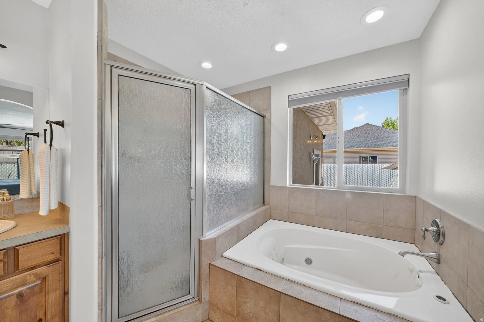 Full-size bathtub with surrounding tile, separate shower enclosure with textured glass, and a large window