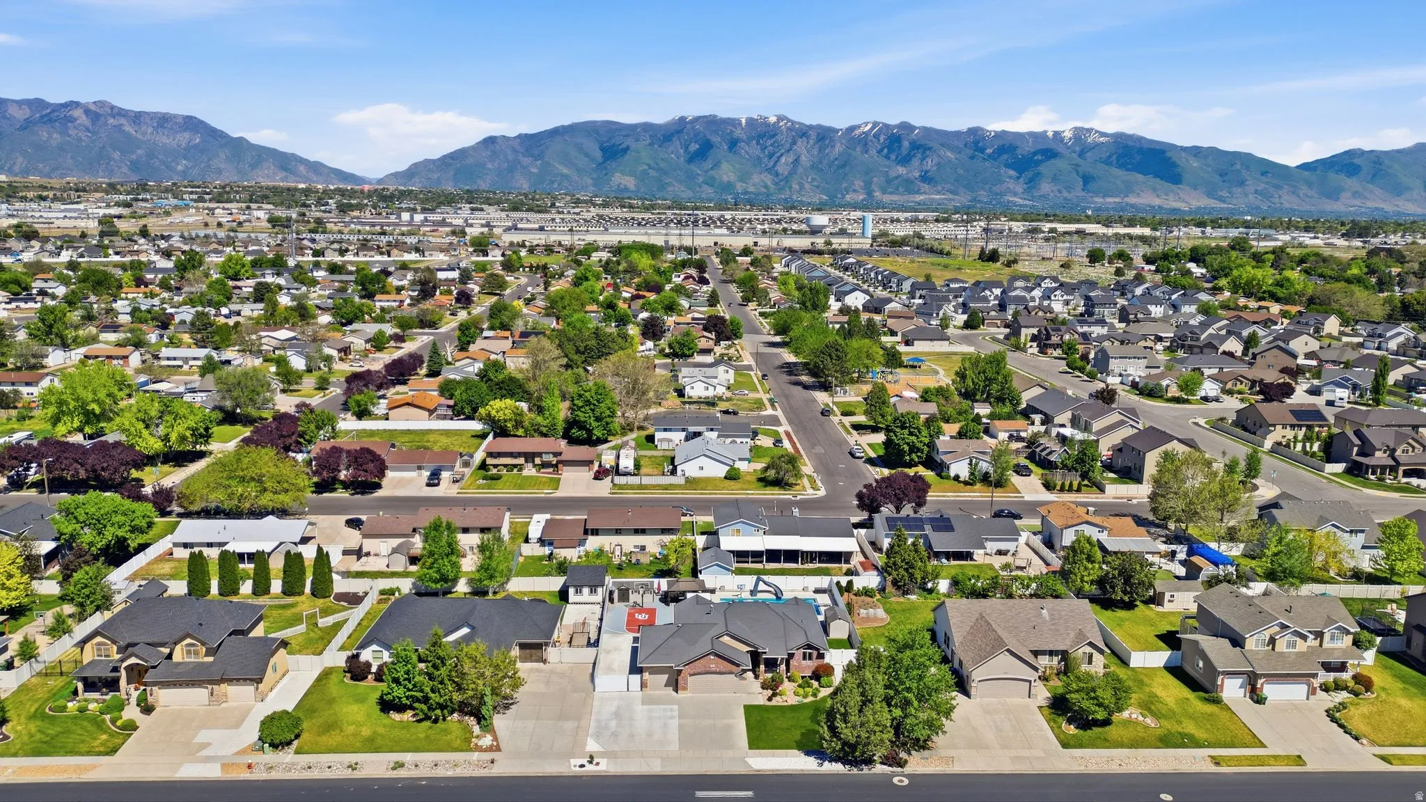 Expansive neighborhood featuring residential properties with pitched roofs, mature trees, and paved streets, set against a backdrop of distant mountains