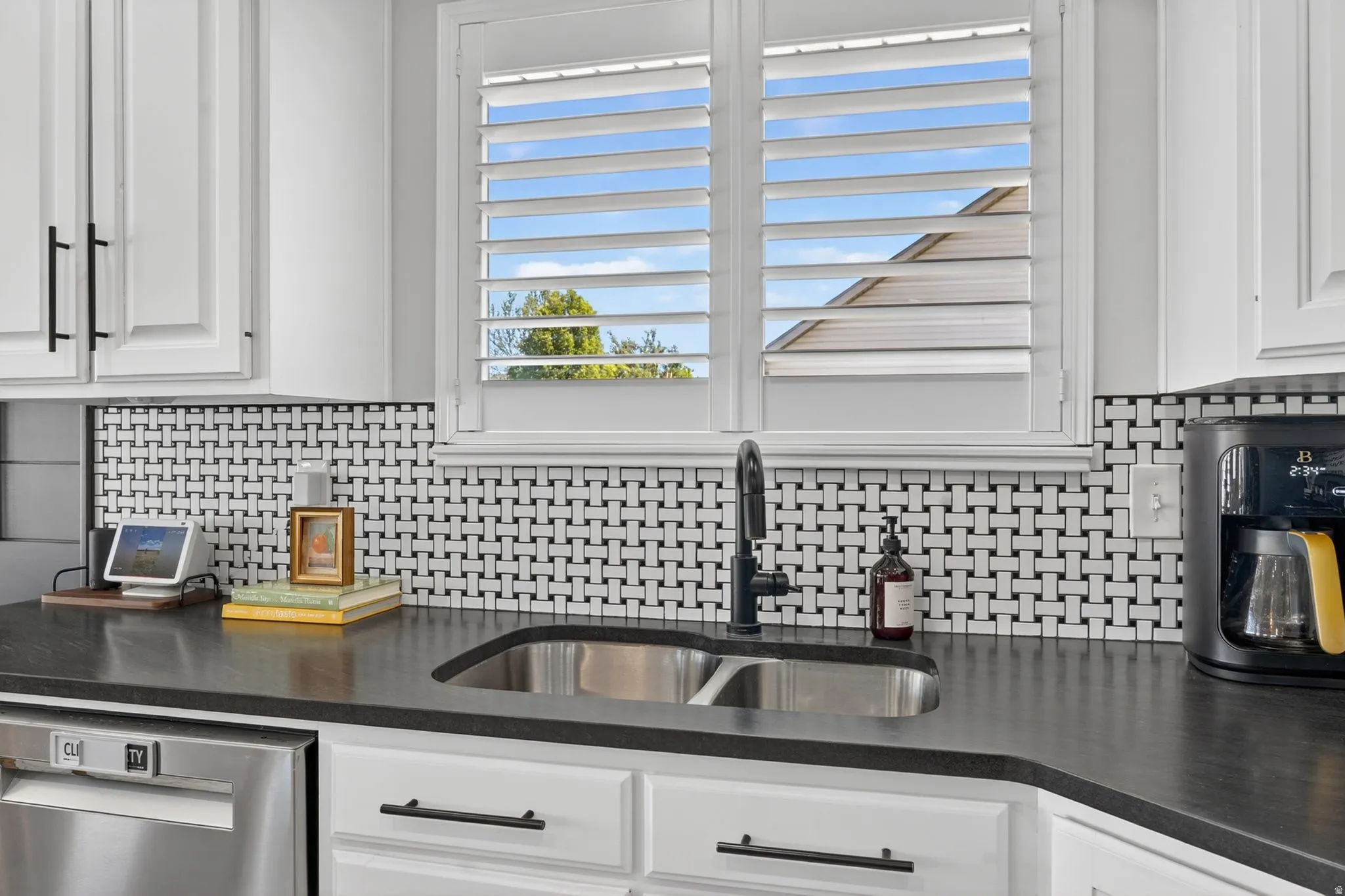 Kitchen featuring white shaker cabinetry, black countertops, stainless steel sink with a matte black faucet, and a basketweave tile backsplash