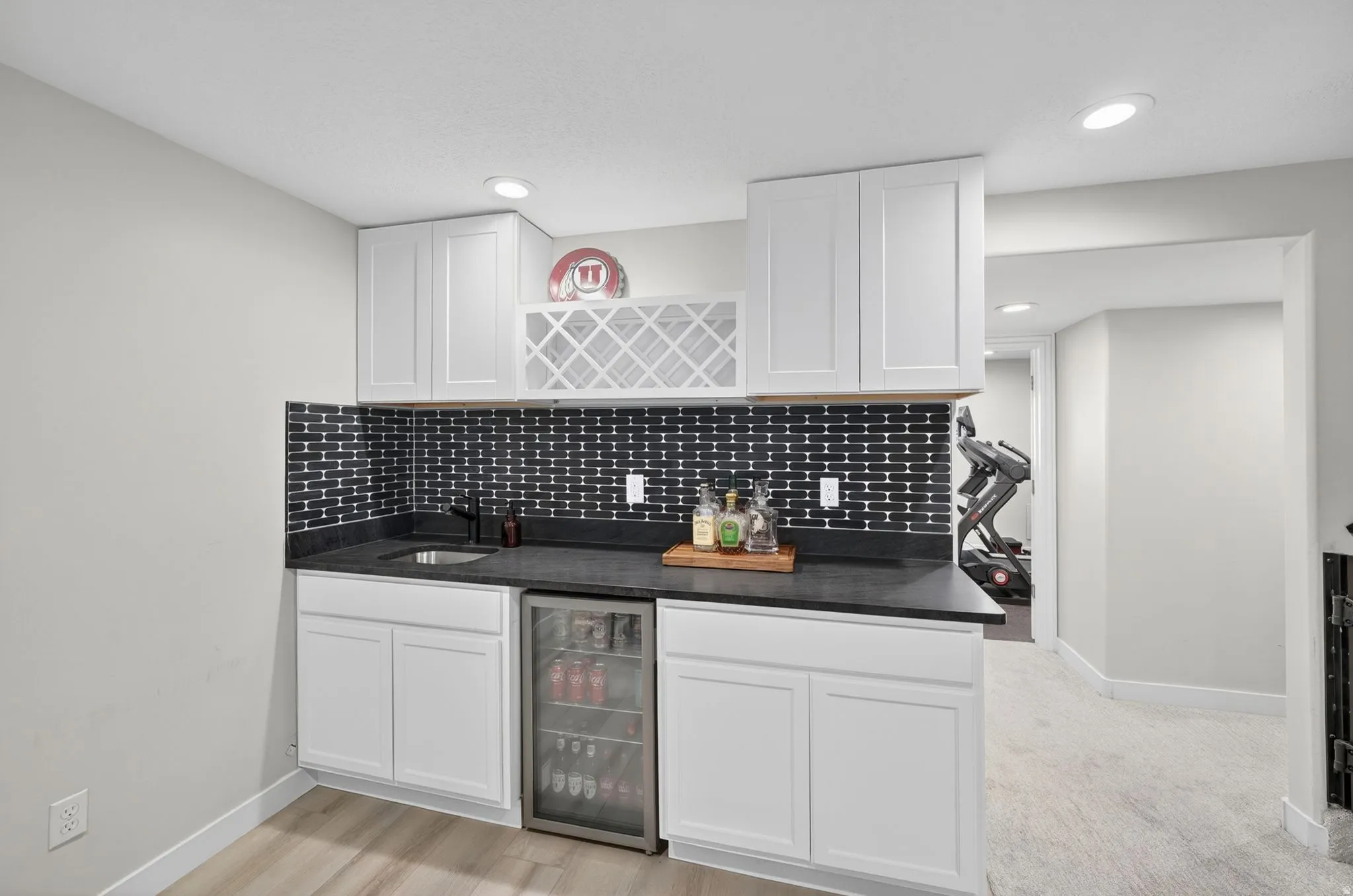 Wet bar featuring white shaker cabinetry, dark countertops, an integrated sink with a matte black faucet, and a beverage refrigerator
