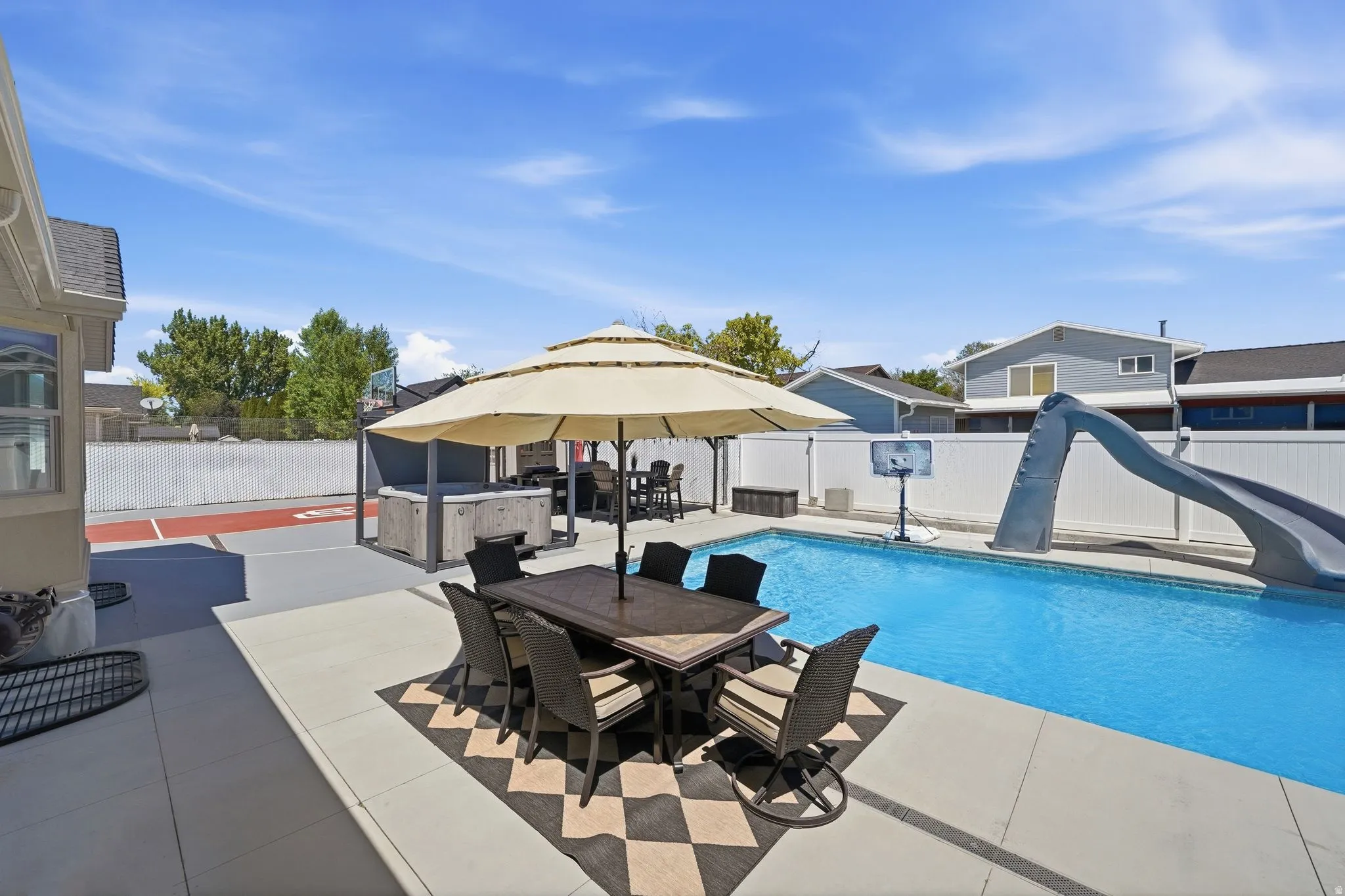 Expansive concrete patio with a built-in outdoor kitchen area, inground swimming pool, and dedicated sports court