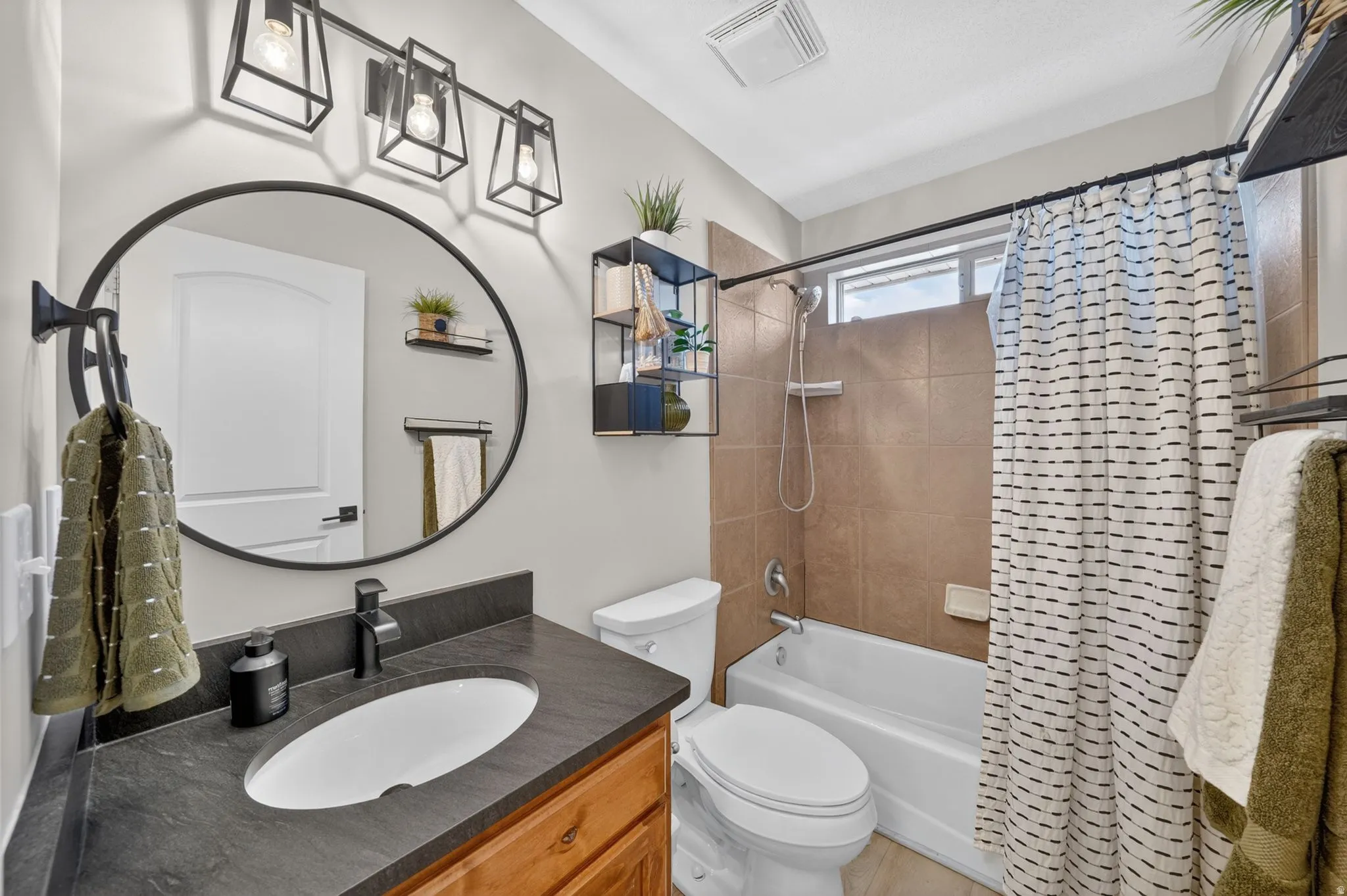 Bathroom featuring a wood-finish vanity with a dark countertop and integrated sink, a large circular mirror, and a three-light vanity fixture
