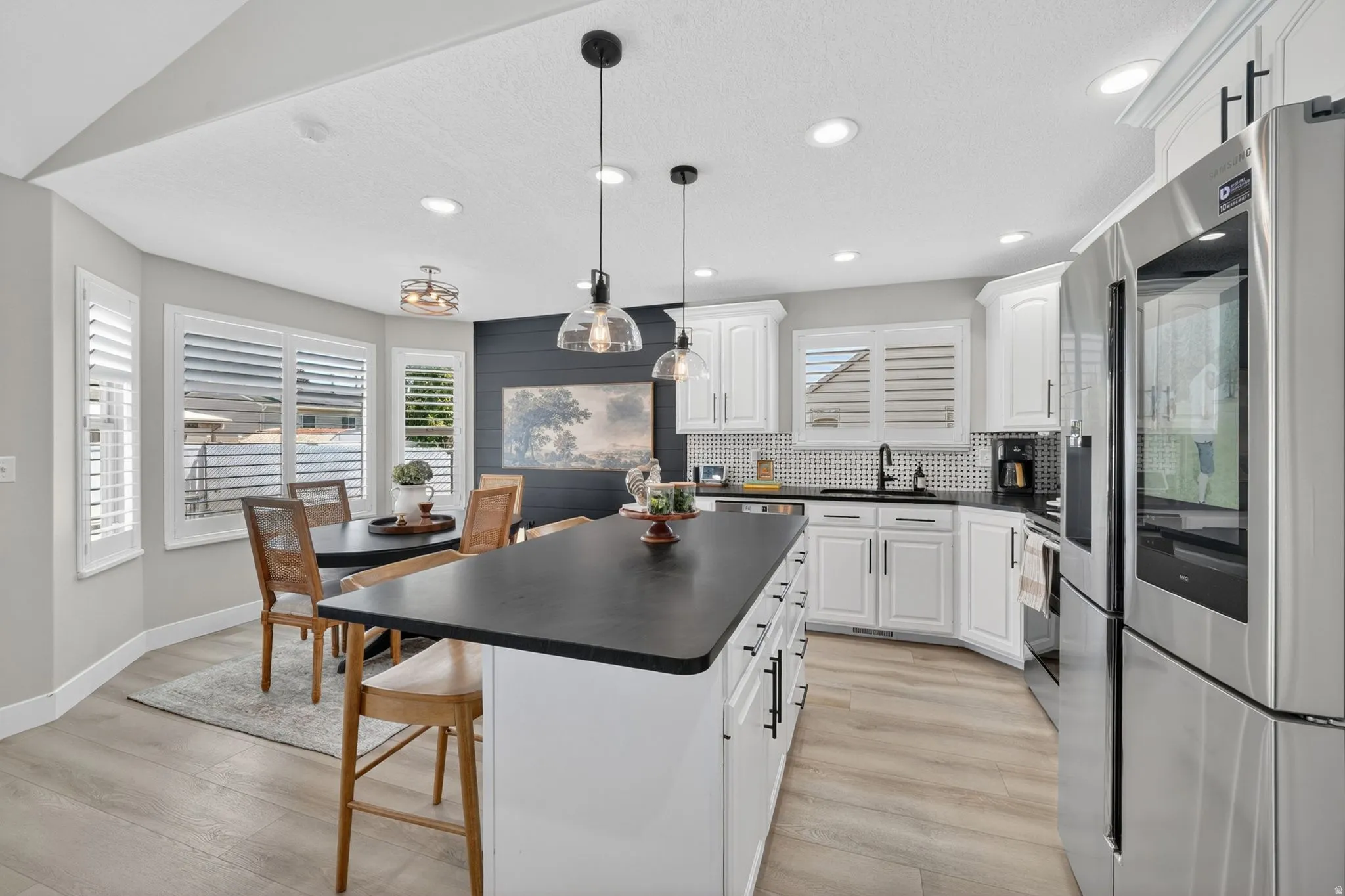 Modern kitchen featuring white cabinetry, a large island with a dark countertop, stainless steel appliances, and wood-finish flooring