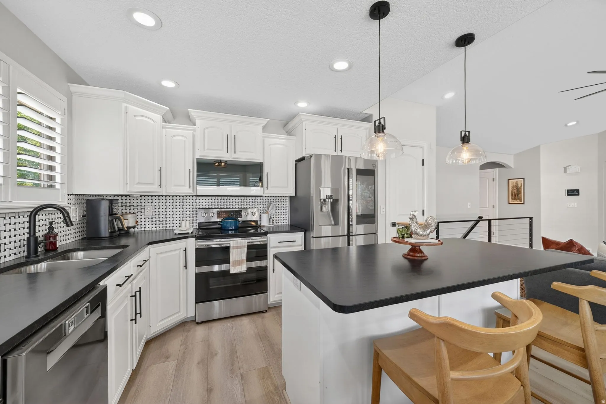 Modern kitchen featuring an island with pendant lighting, white cabinetry, dark countertops, a patterned tile backsplash, and stainless steel appliances