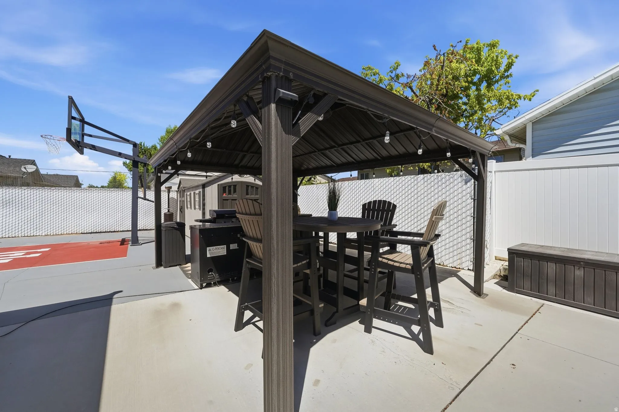 Patio featuring a dark-toned gazebo with string lighting, concrete flooring, and a privacy fence