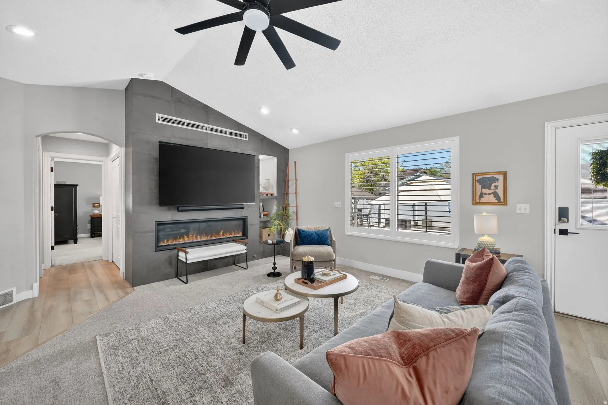 Spacious living area featuring a vaulted ceiling with a ceiling fan, a contemporary fireplace with a sleek surround, wood-finish flooring, and ample natural light from a large window