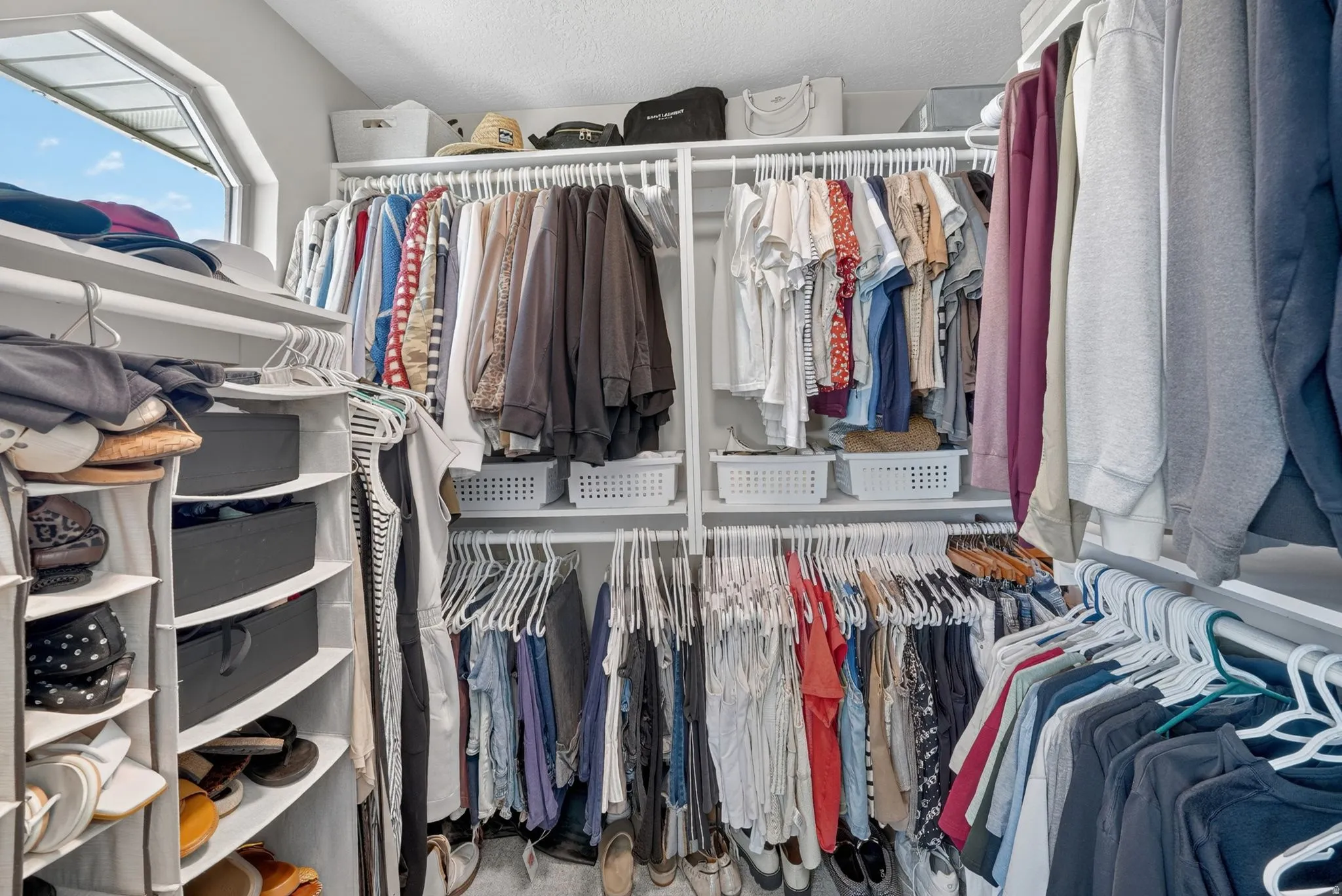 Custom closet system featuring multiple hanging rods, integrated shelving units, and an angled window for natural light