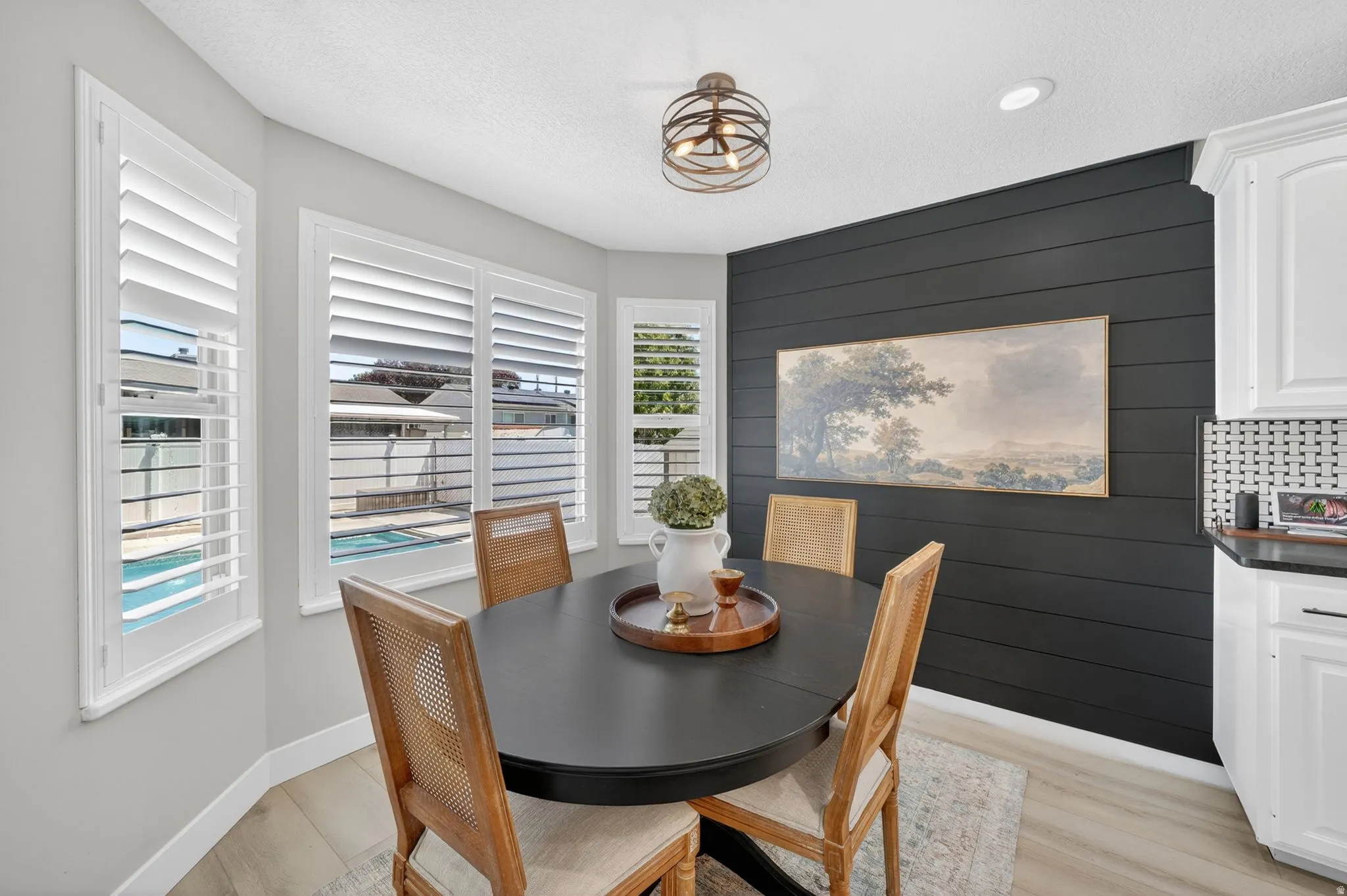 Bay window with plantation shutters, light wood-finish flooring, a shiplap accent wall, white cabinetry, and a black and white tiled backsplash