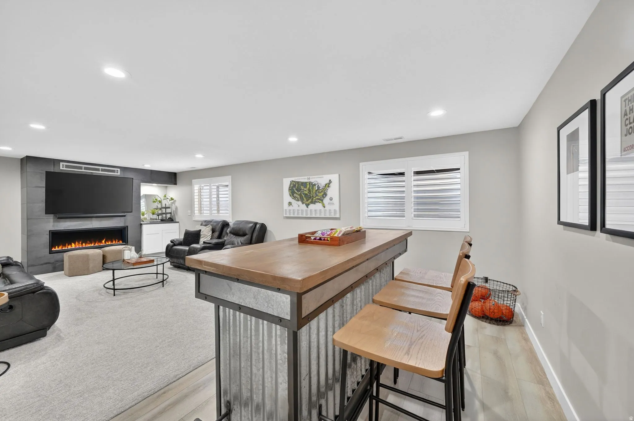 Entertainment area featuring a wood-top bar with a corrugated metal base, recessed lighting, and a modern linear fireplace with a tile surround