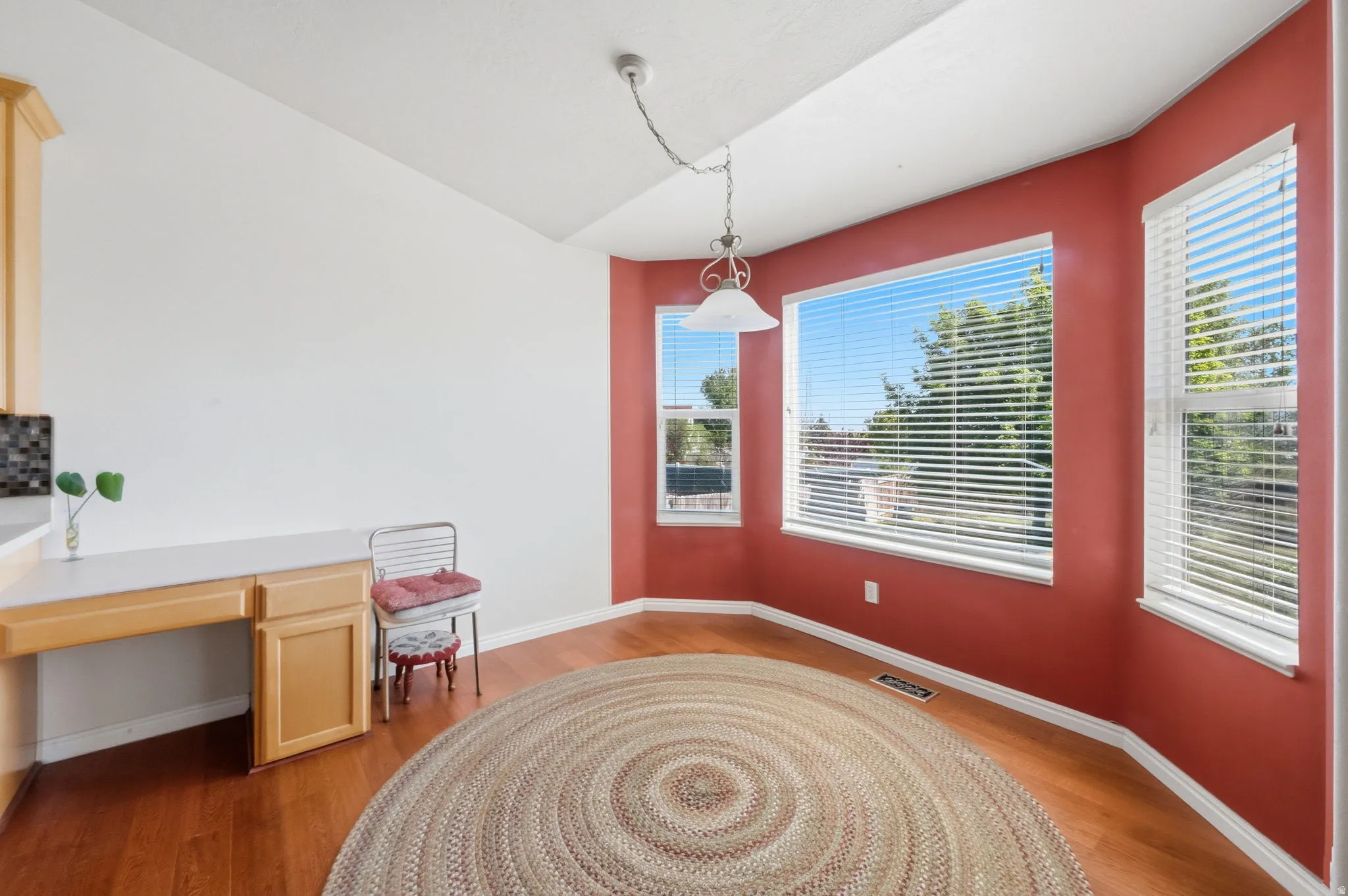 Dining area featuring an angled vaulted ceiling, a built-in desk with cabinetry, a tiled backsplash, and multiple windows with horizontal blinds