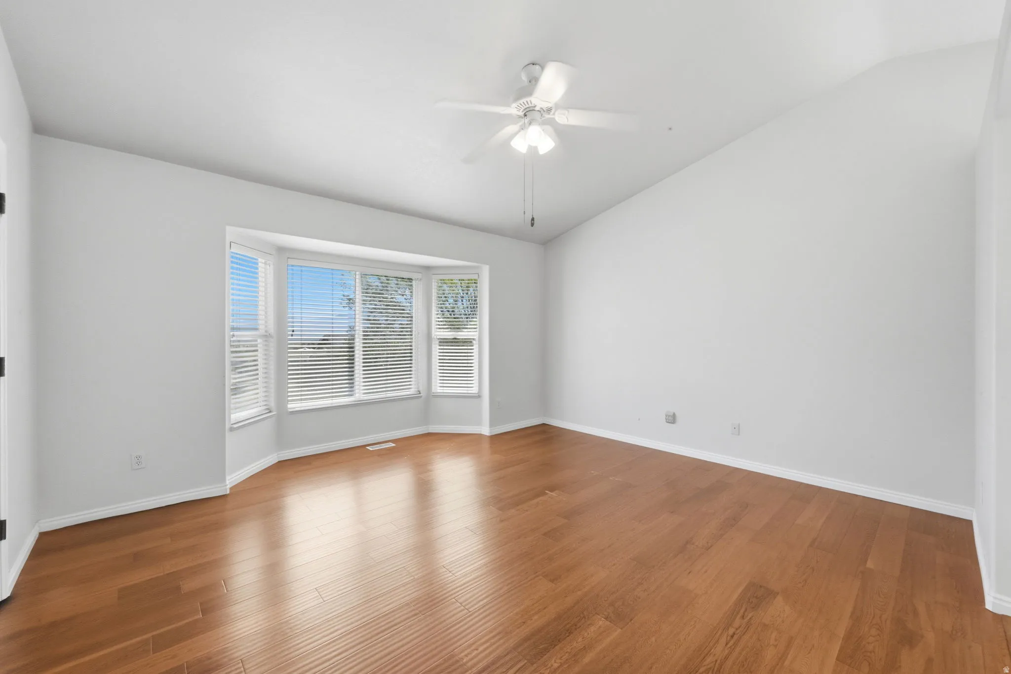 Spacious room featuring wood-finish flooring and a prominent bay window with white blinds