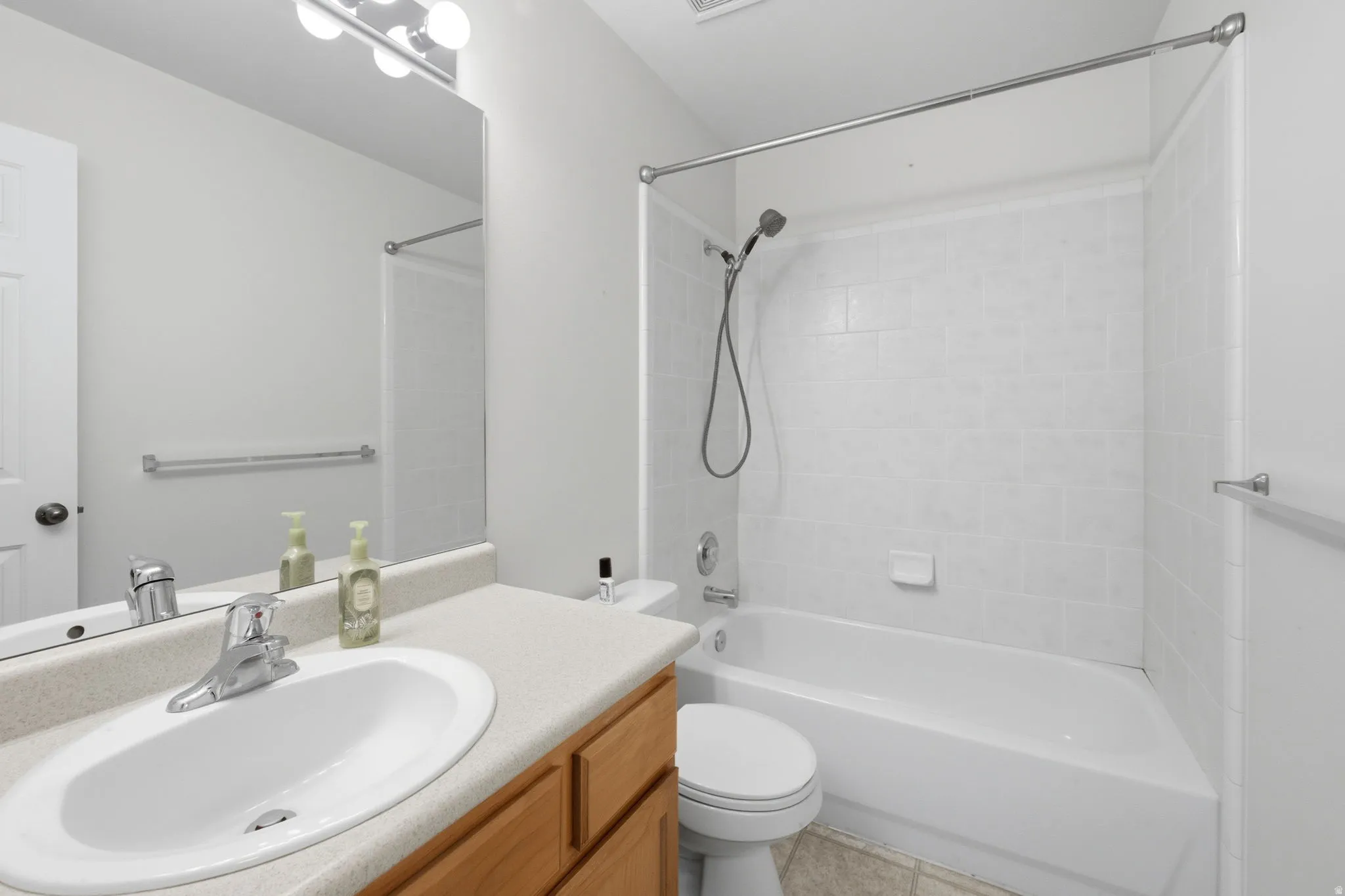 Full bathroom featuring a single vanity with wood-finish cabinetry, a large mirror, a chrome faucet, and overhead lighting