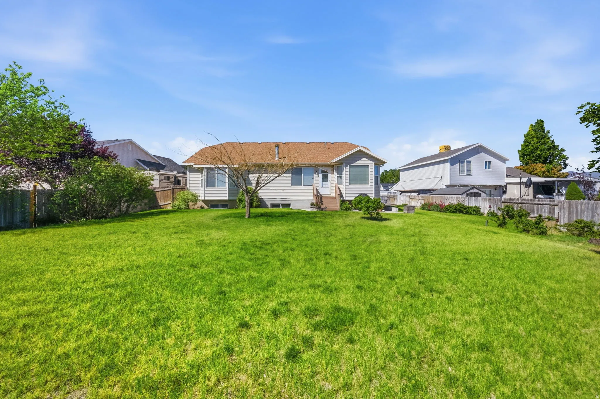 Expansive grassy yard with mature landscaping and a partial privacy fence