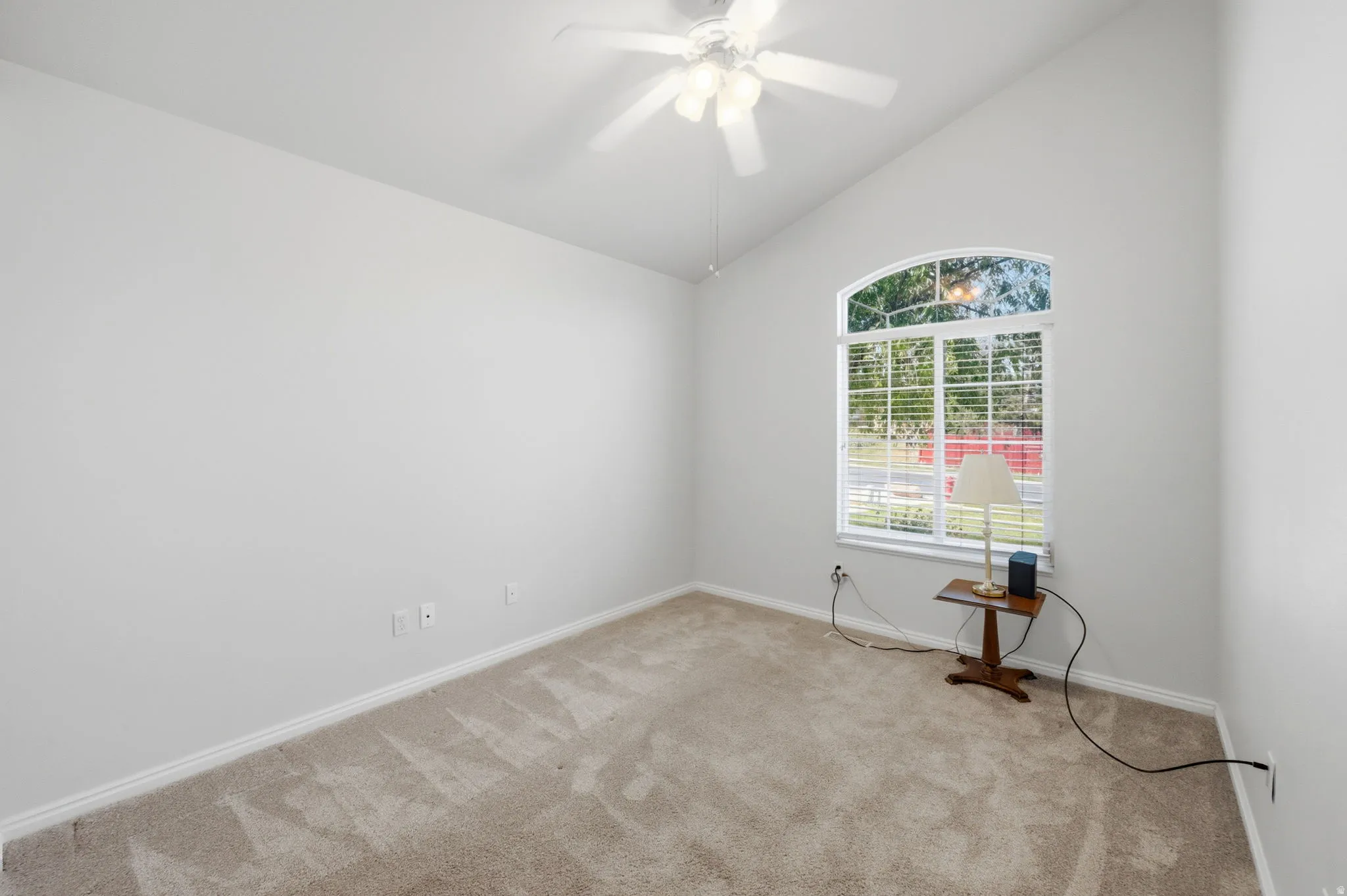 Vaulted ceiling with a ceiling fan, arched window with horizontal blinds, neutral-toned carpeting, and crisp white baseboards