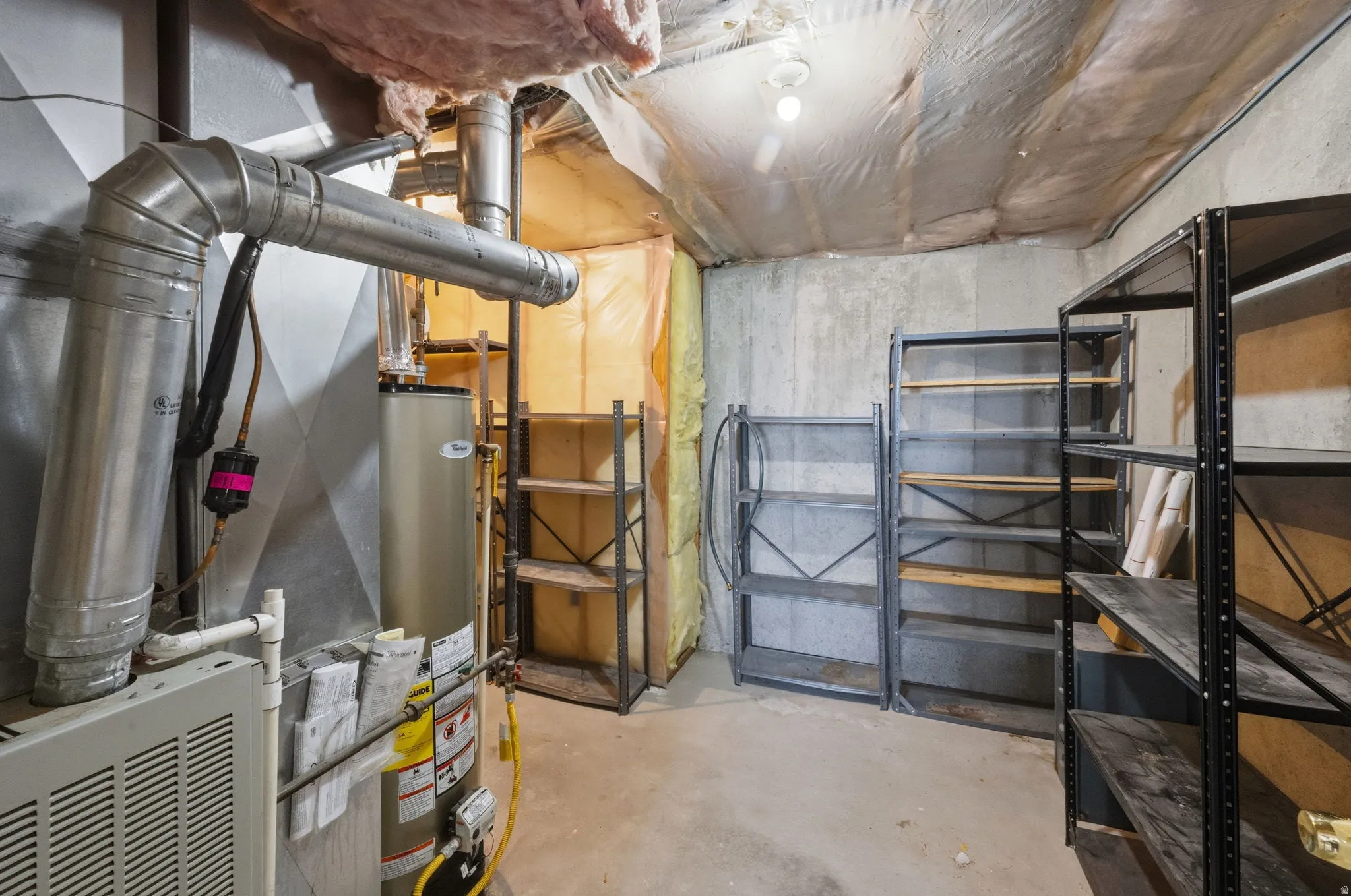 Basement utility area featuring a water heater, furnace, exposed ductwork, concrete walls, and multiple metal shelving units for storage