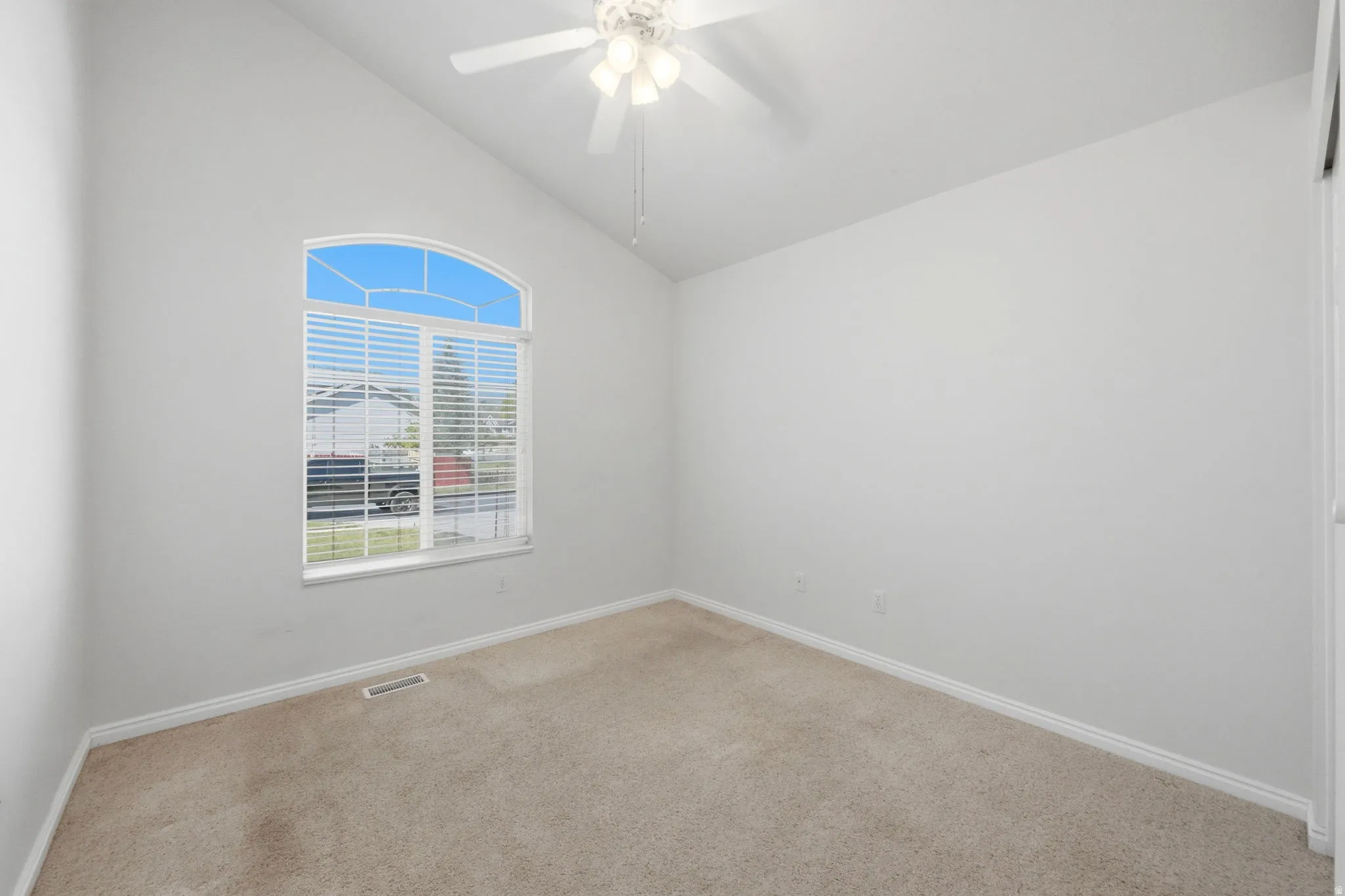 Room featuring a vaulted ceiling and a large arched window with blinds