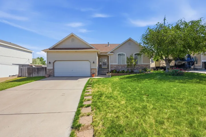 Ranch-style exterior featuring a two-car garage, stone accent siding, arched window details, and a front lawn with mature trees