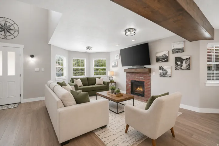 Spacious living area featuring a prominent brick fireplace with a wood mantel, wood-finish flooring, and a vaulted ceiling