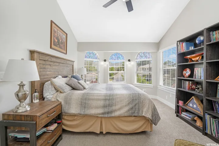 Vaulted ceiling room featuring a ceiling fan, three arched windows with blinds, a rectangular window with blinds, and built-in shelving
