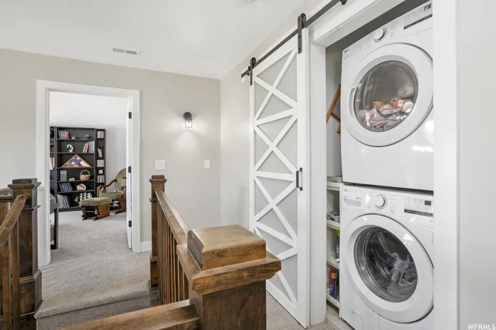Integrated laundry closet featuring a stacked washer and dryer, complete with a contemporary barn door on a black rail