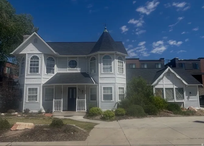 Victorian-style residence with a prominent turret, multiple arched and octagonal windows, a covered front porch, and detailed siding