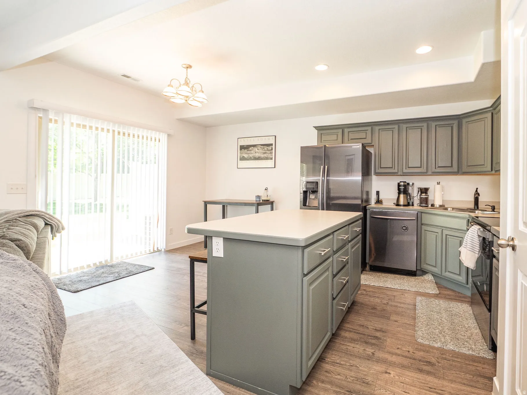 Open-concept living area featuring a kitchen island with integrated storage, wood-finish flooring, a full suite of stainless steel appliances, and sliding glass doors leading to exterior space
