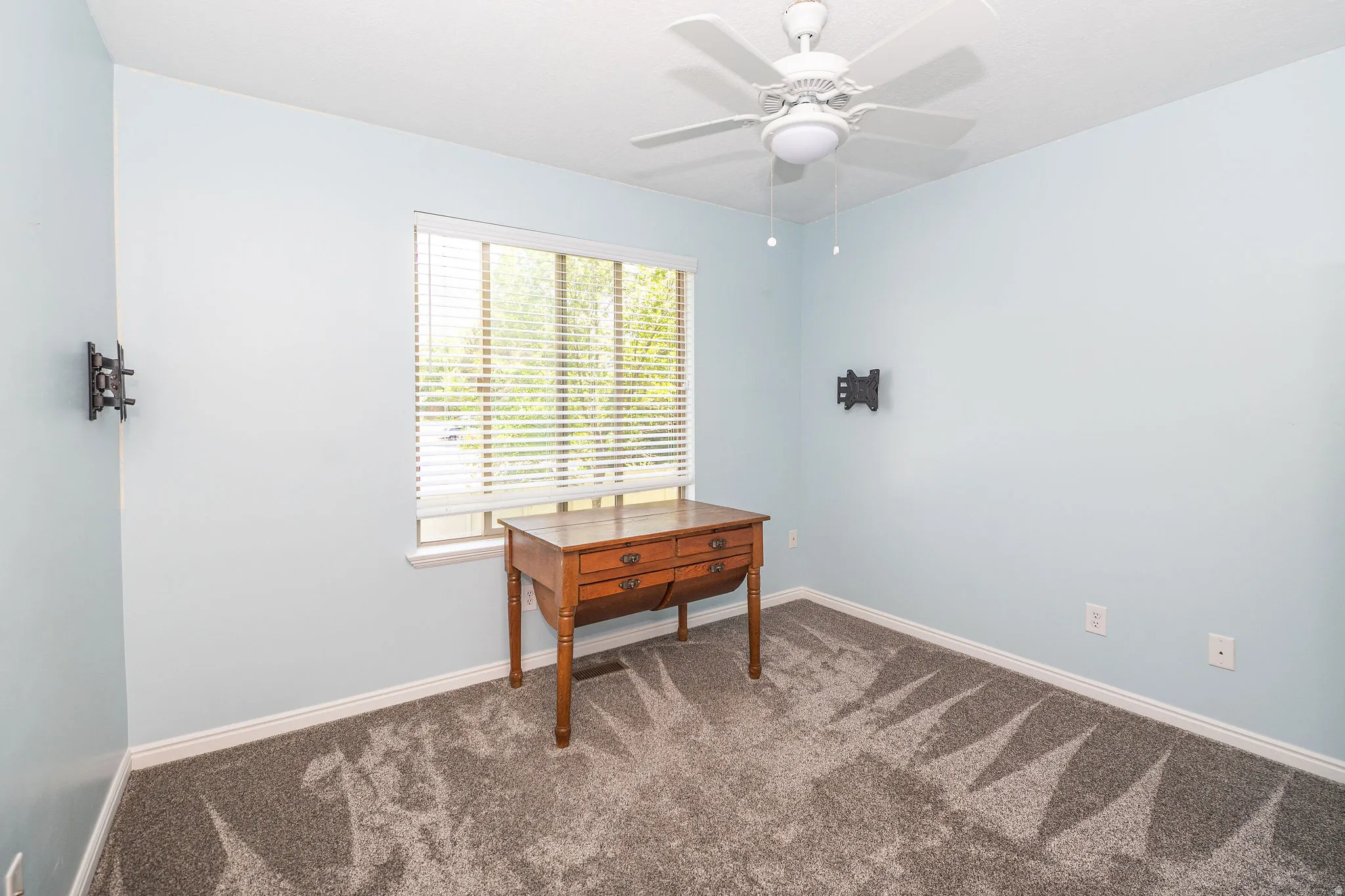 Spacious interior room featuring light blue walls, grey patterned carpet, a single window with blinds, and white trim