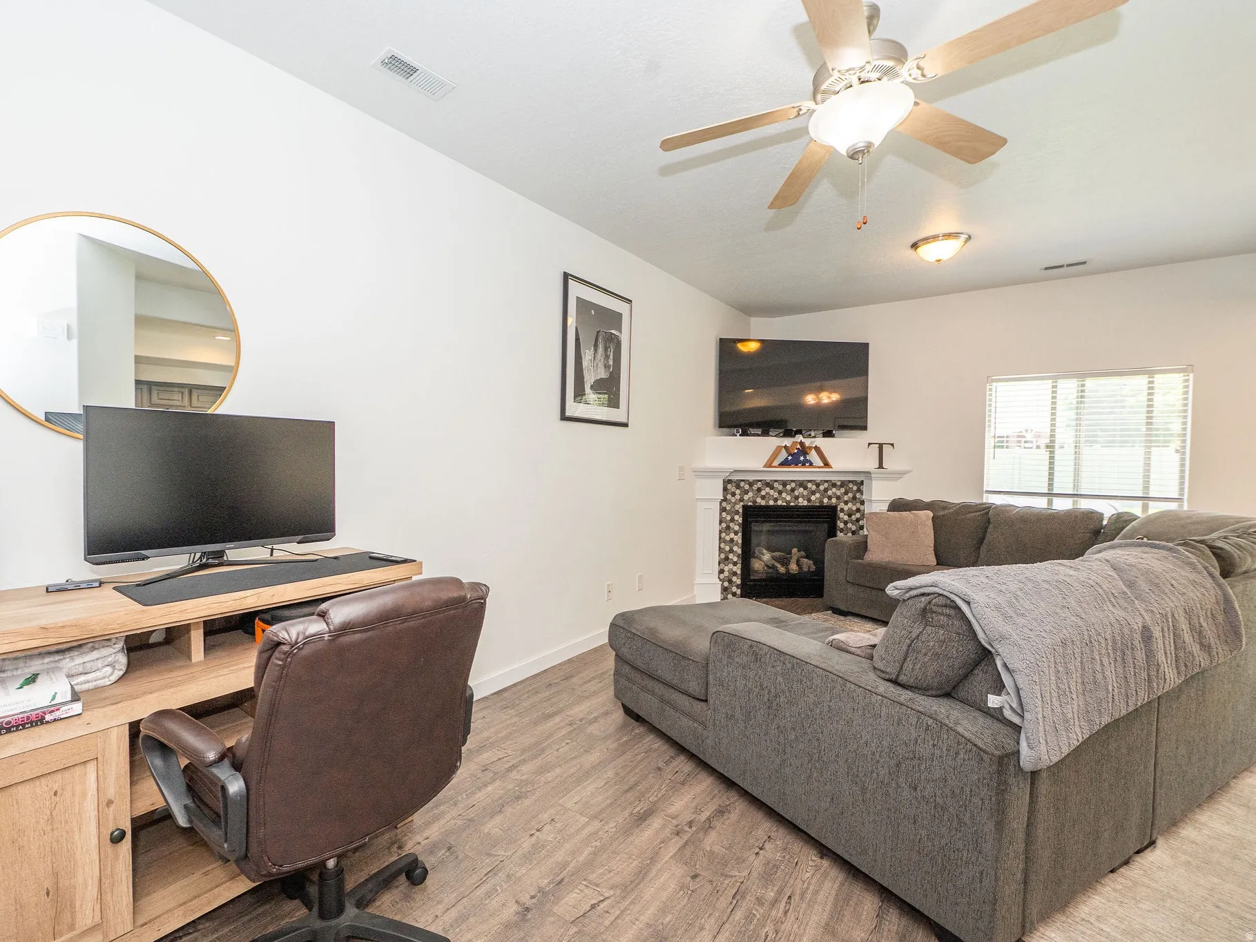 Living area featuring wood-finish flooring, a ceiling fan with light fixture, and a fireplace with a decorative tile surround and white mantel