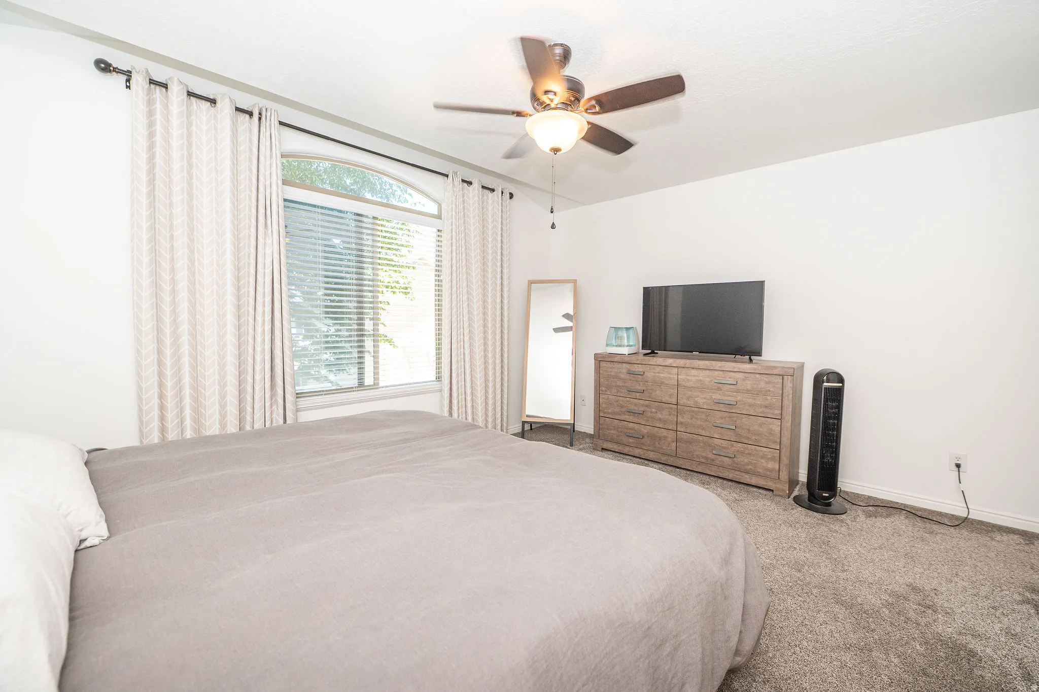 Bedroom featuring an arched window with blinds, ceiling fan with integrated lighting, and neutral-toned carpeting