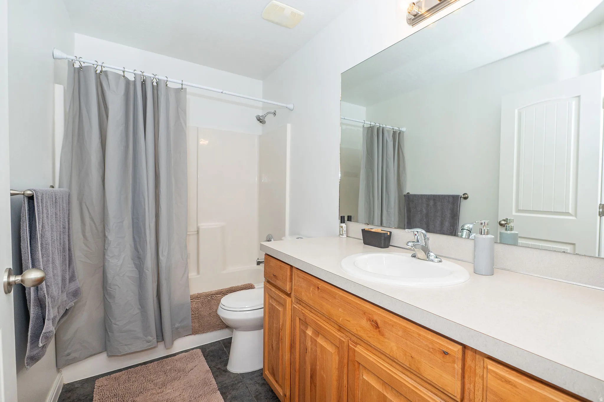 Bathroom featuring a wood-finish vanity with a light countertop, an integrated sink, and a large wall-mounted mirror