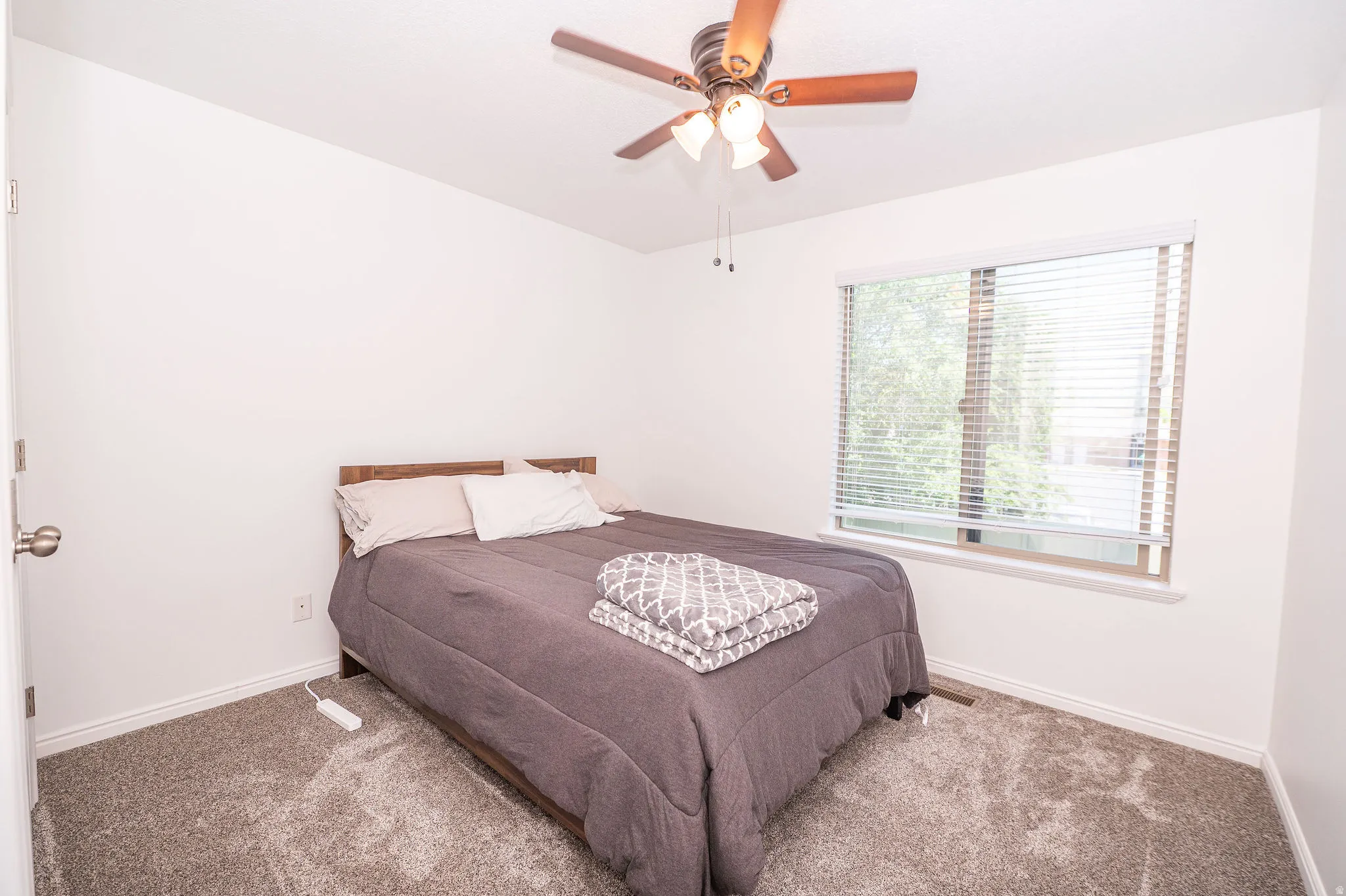 Carpeted room featuring a ceiling fan with integrated lighting, a window with blinds, and white baseboards