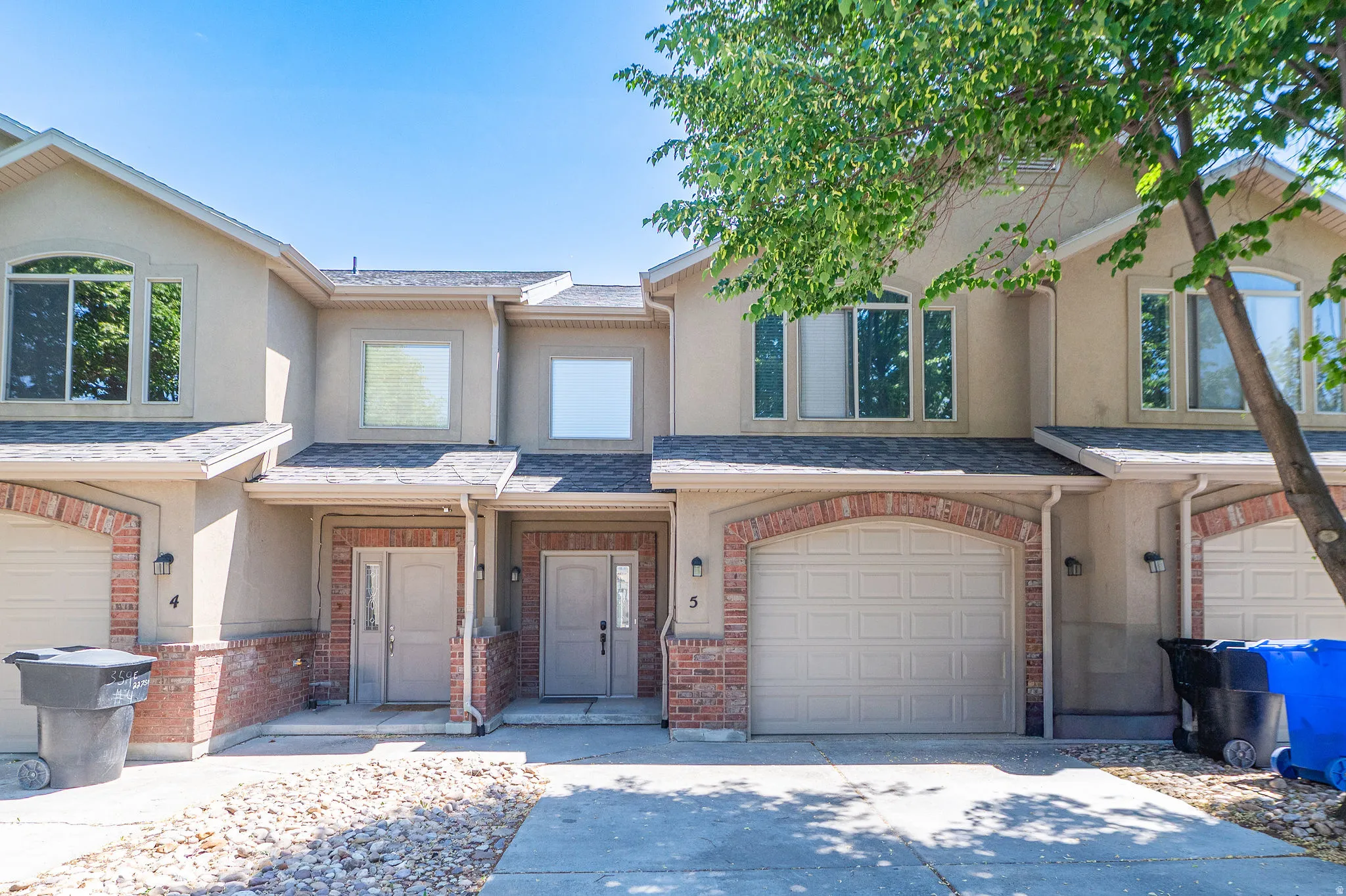 Stucco townhome exterior featuring an arched brick garage surround, neutral tone garage door, double-pane windows, and a paved driveway