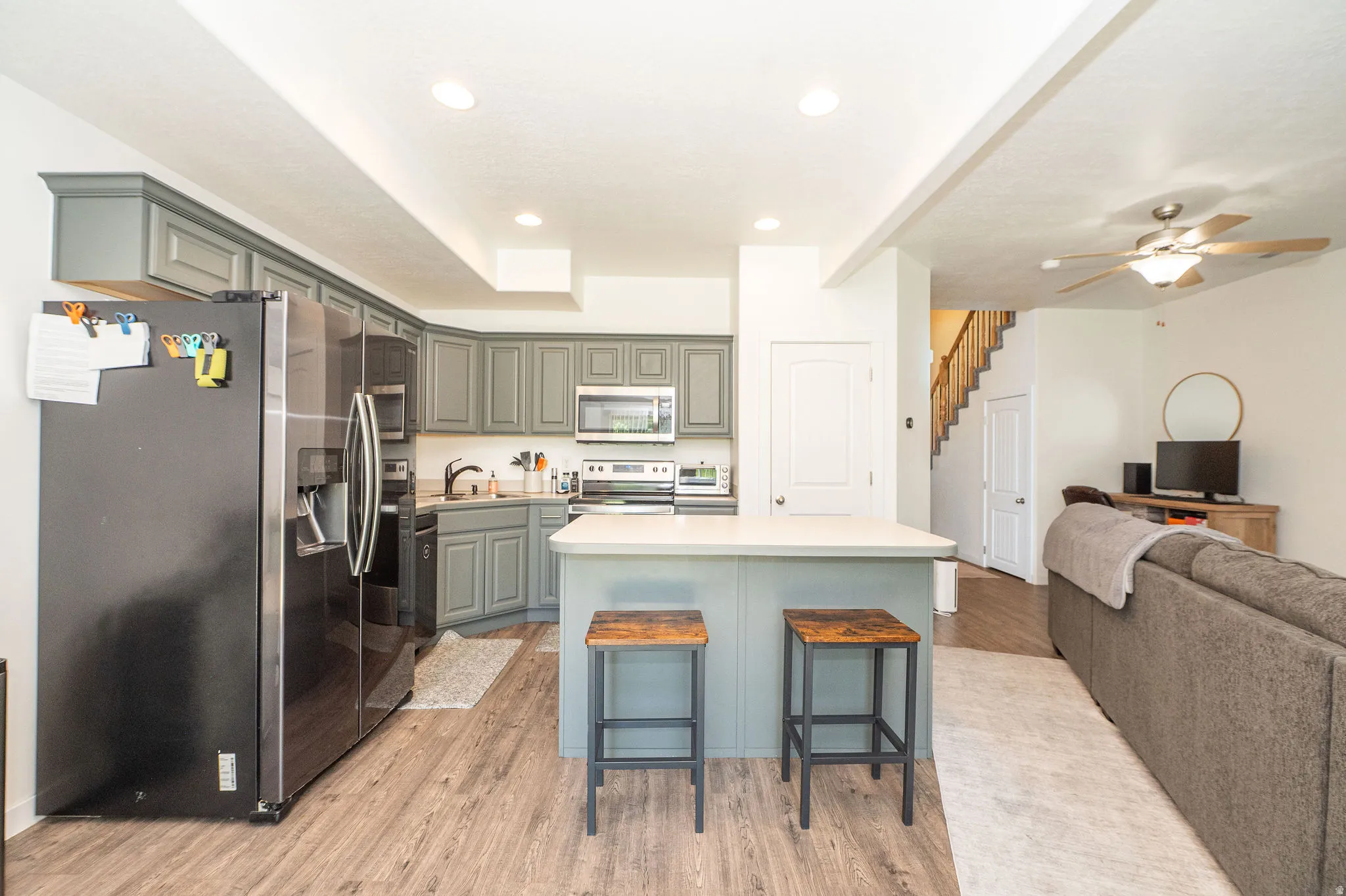 Open-concept kitchen featuring gray cabinetry, stainless steel appliances, and a central island with countertop seating