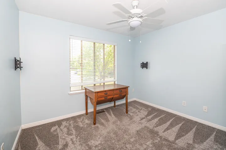 Spacious interior room featuring light blue walls, grey patterned carpet, a single window with blinds, and white trim