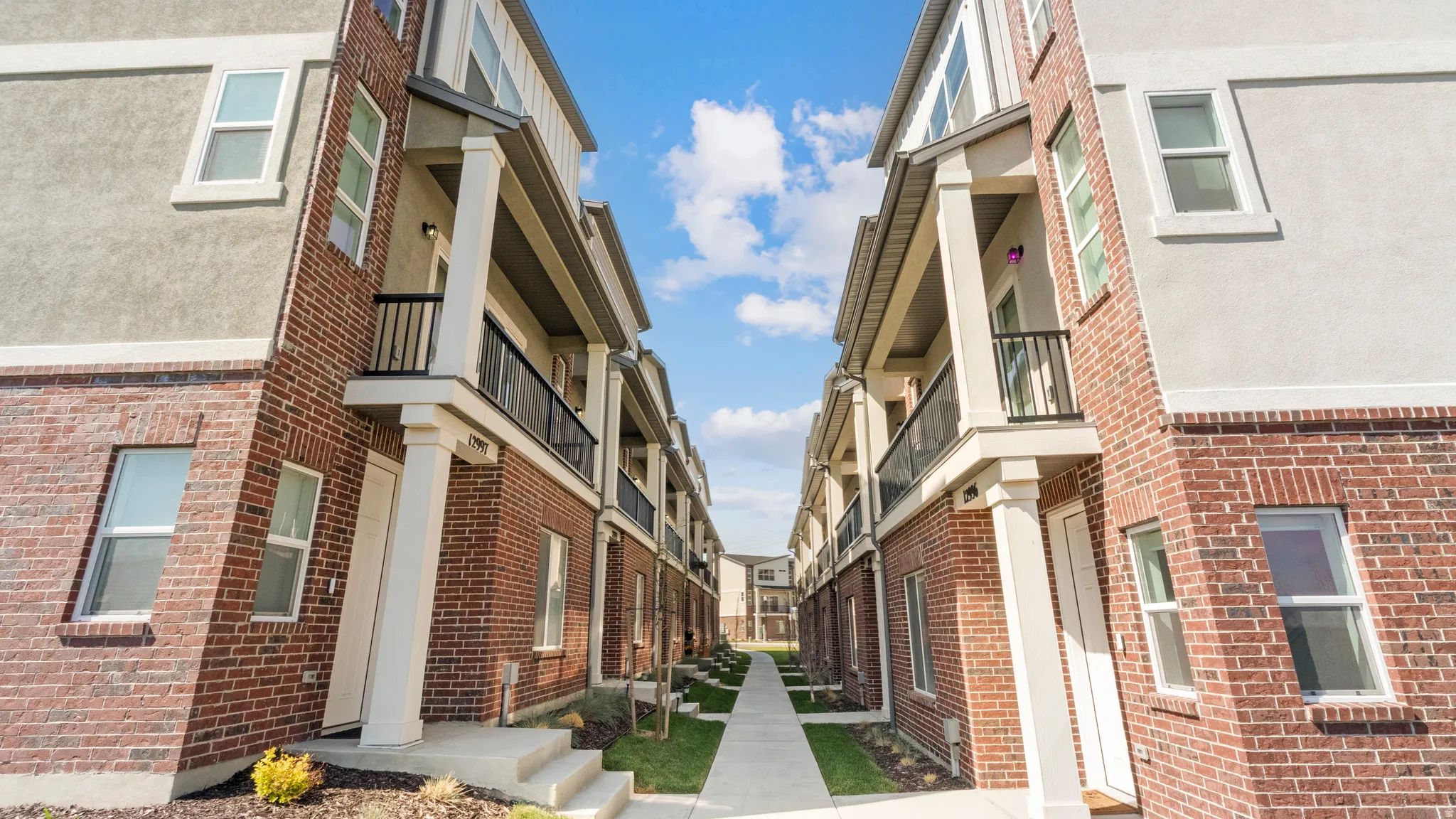 Modern townhome-style exterior featuring a red brick facade with stucco accents, white-framed windows, and a private balcony with black railings