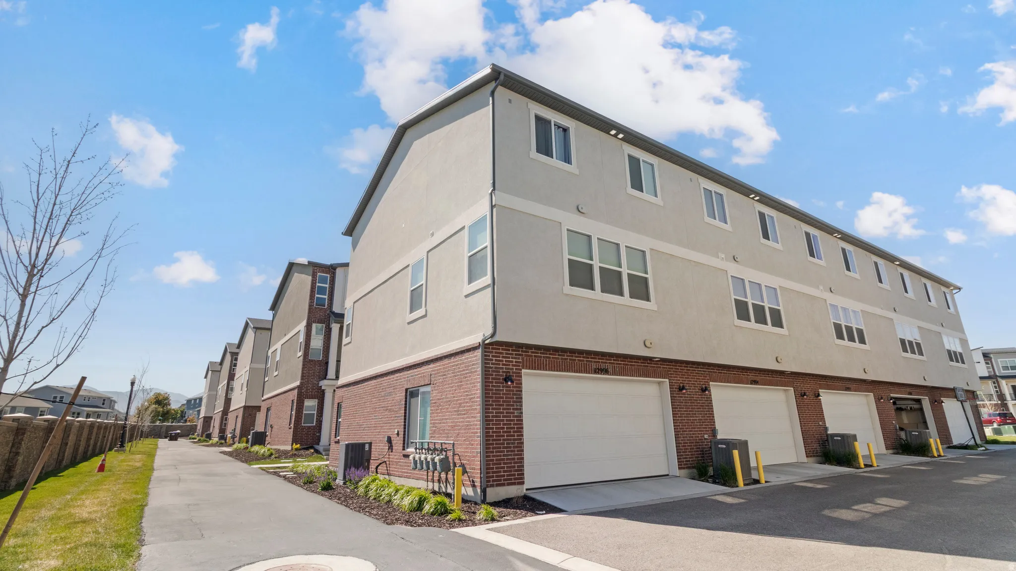 Multi-level townhome exterior featuring an attached two-car garage, brick veneer siding, and stucco finishes