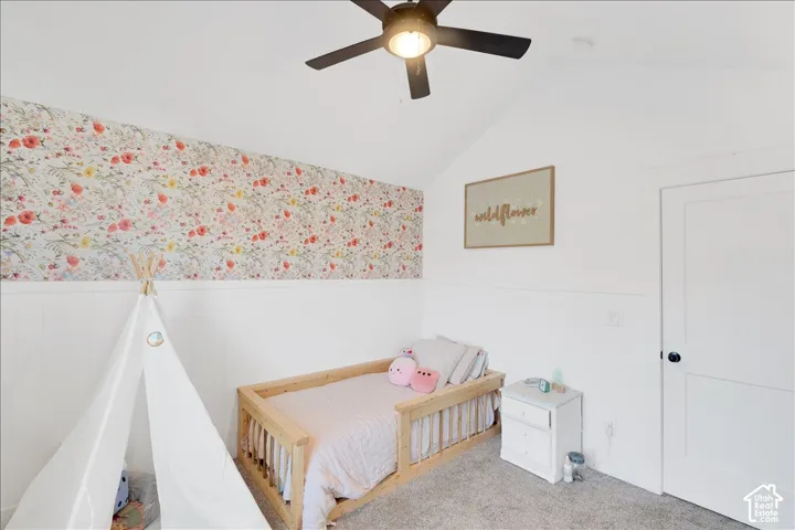 Interior room featuring a vaulted ceiling with a ceiling fan, white paneled walls, and a floral accent wall