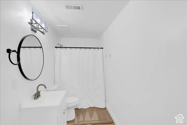 Bathroom with a white vanity, a round black-framed mirror, a brushed nickel faucet, a white shower curtain with a black rod, and light wood-finish flooring