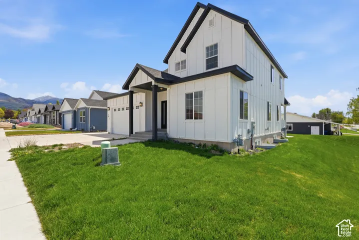 Modern farmhouse-style residence featuring white vertical siding, black trim accents, a covered entry, an attached two-car garage, and a lush green lawn