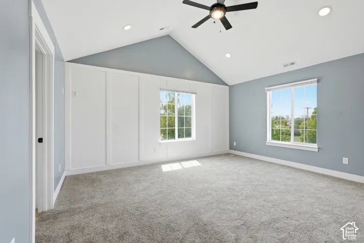 Spacious interior room featuring a vaulted ceiling with a ceiling fan, recessed lighting, two large windows, white trim, and light gray carpeting