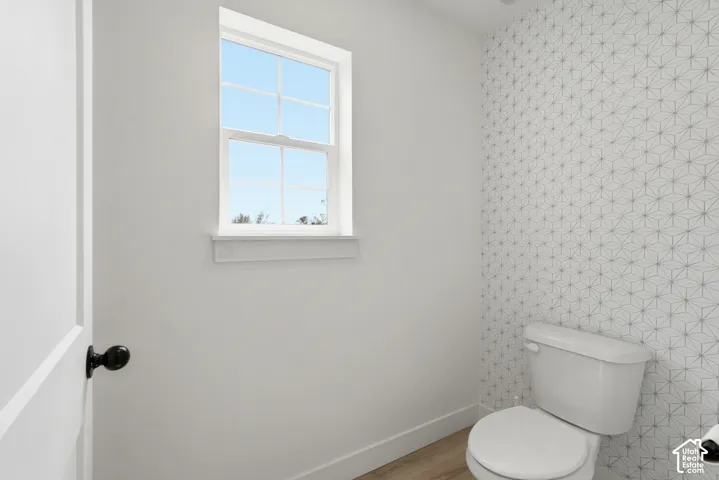 Powder room featuring a geometric patterned accent wall, single-pane window, white trim, and wood-finish flooring