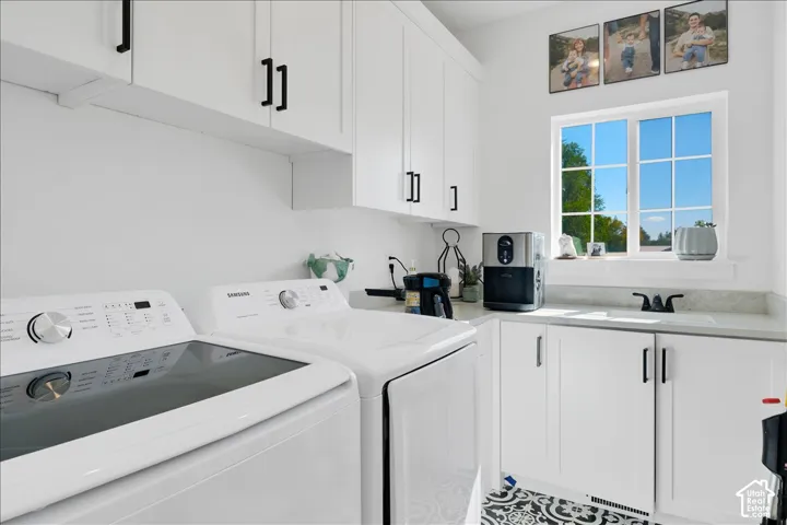 Dedicated utility space featuring white cabinetry with black hardware, a window, a single basin sink with a black faucet, and patterned floor tiling